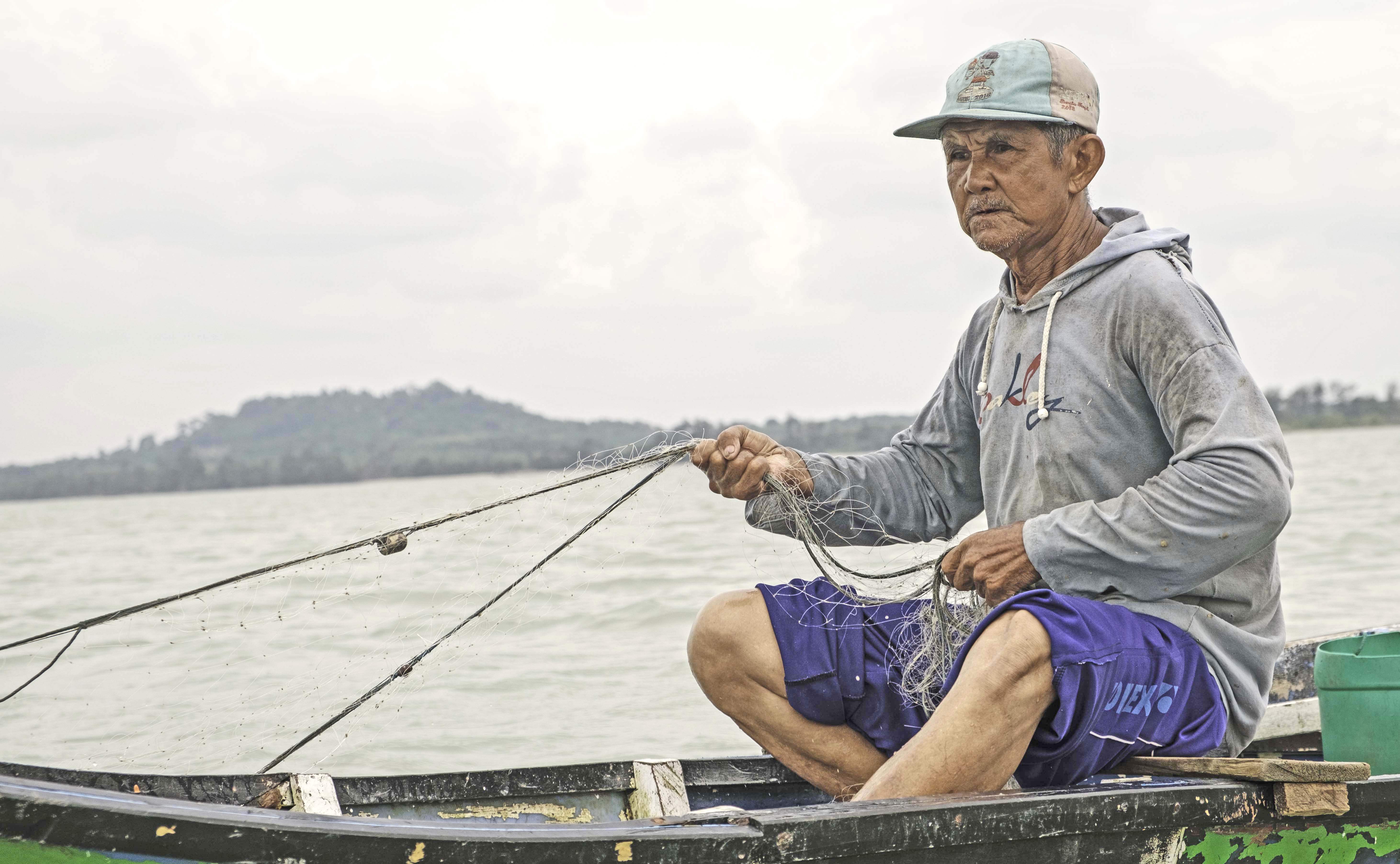 A fisherman in a baseball cap holds onto a net in a small wooden boat